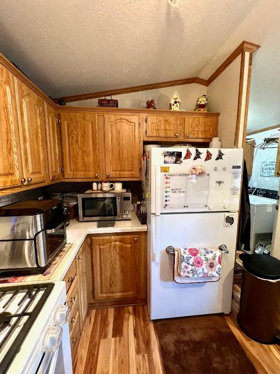 kitchen with white appliances, light hardwood / wood-style flooring, vaulted ceiling, ornamental molding, and a textured ceiling