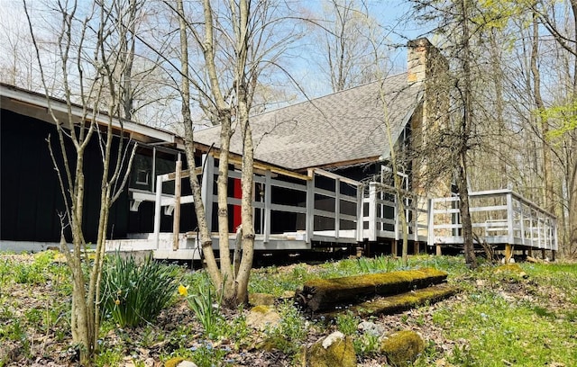 rear view of property with a shingled roof, a sunroom, a deck, and a chimney