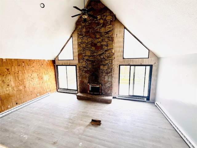 unfurnished living room with ceiling fan, baseboard heating, a wood stove, high vaulted ceiling, and wood finished floors