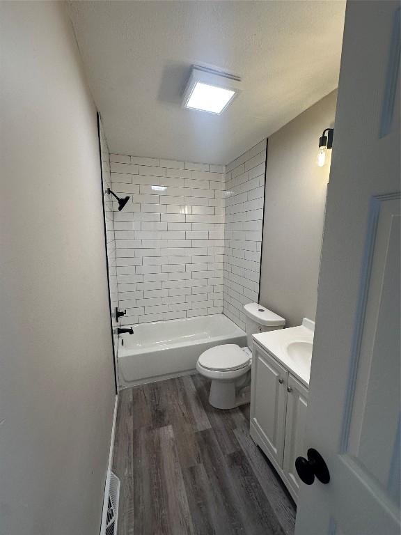 full bathroom with vanity, wood-type flooring, a textured ceiling, tiled shower / bath, and toilet