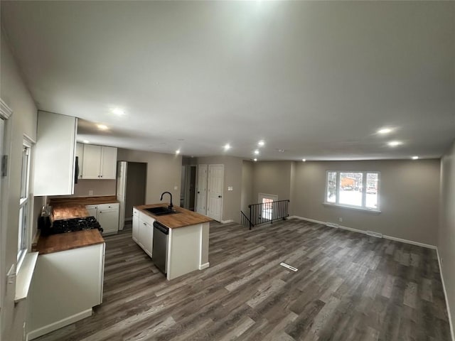 kitchen featuring an island with sink, butcher block counters, sink, dark hardwood / wood-style flooring, and stainless steel dishwasher