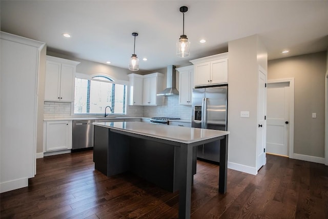 kitchen with a center island, wall chimney range hood, decorative light fixtures, white cabinets, and appliances with stainless steel finishes