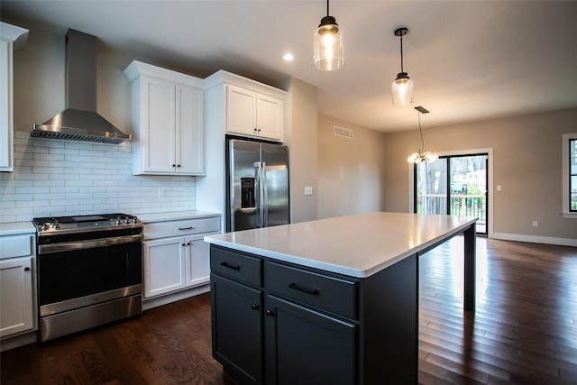 kitchen with decorative backsplash, appliances with stainless steel finishes, wall chimney exhaust hood, white cabinetry, and hanging light fixtures