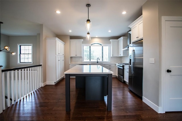 kitchen featuring appliances with stainless steel finishes, backsplash, decorative light fixtures, white cabinetry, and a kitchen island