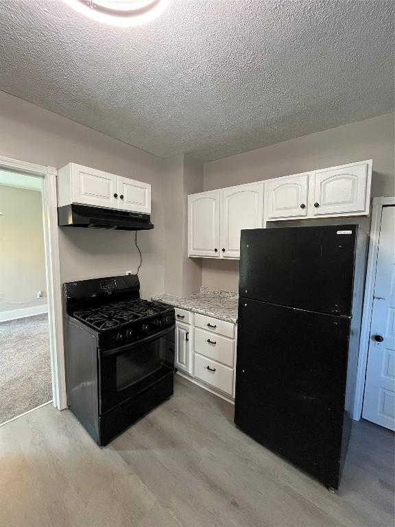 917 Walnut St, Erie, PA 16502 - kitchen with black appliances, under cabinet range hood, light wood-style flooring, a textured ceiling, and white cabinetry