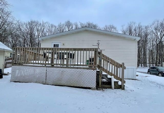 snow covered back of property with a wooden deck