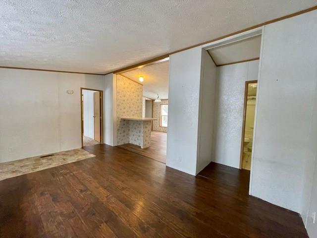 spare room featuring ornamental molding, vaulted ceiling, a textured ceiling, and wood finished floors