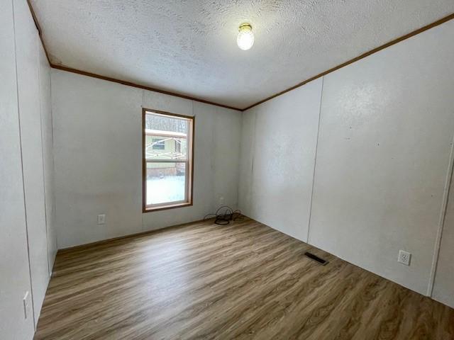 empty room featuring visible vents, crown molding, and wood finished floors