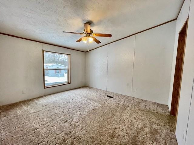 carpeted spare room featuring a textured ceiling, ornamental molding, and a ceiling fan