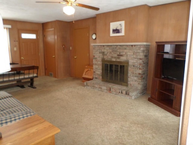 carpeted living room featuring a fireplace, wooden walls, and ceiling fan