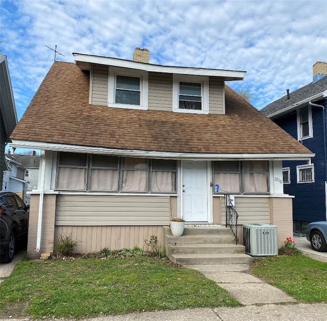 view of front facade with a chimney, central AC unit, entry steps, and a shingled roof