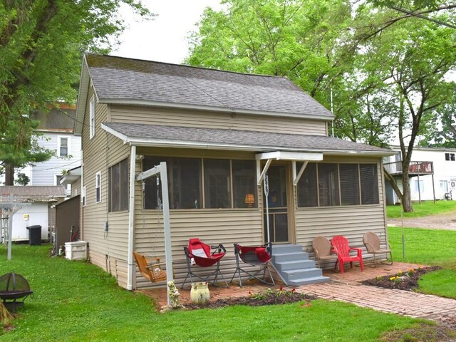 10987 Henry St, Conneaut Lake, PA 16316 - view of front of house featuring a sunroom, a shingled roof, a front yard, and entry steps