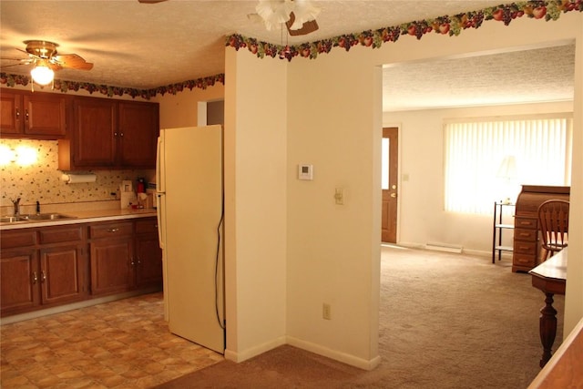 kitchen featuring light carpet, white refrigerator, sink, ceiling fan, and a textured ceiling