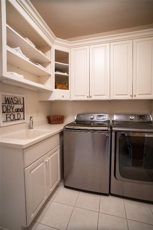 laundry room with cabinets, light tile patterned floors, washing machine and dryer, and sink