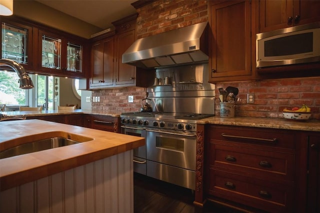 kitchen featuring butcher block counters, sink, stainless steel appliances, wall chimney range hood, and decorative backsplash