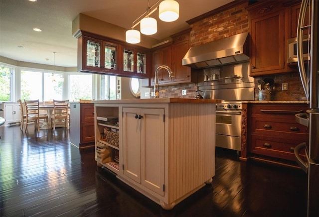 kitchen with decorative backsplash, dark wood-type flooring, wall chimney range hood, decorative light fixtures, and an island with sink