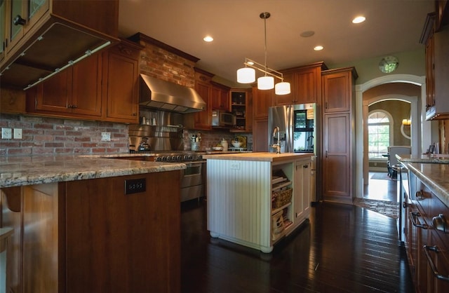 kitchen with appliances with stainless steel finishes, pendant lighting, dark hardwood / wood-style flooring, and wall chimney exhaust hood