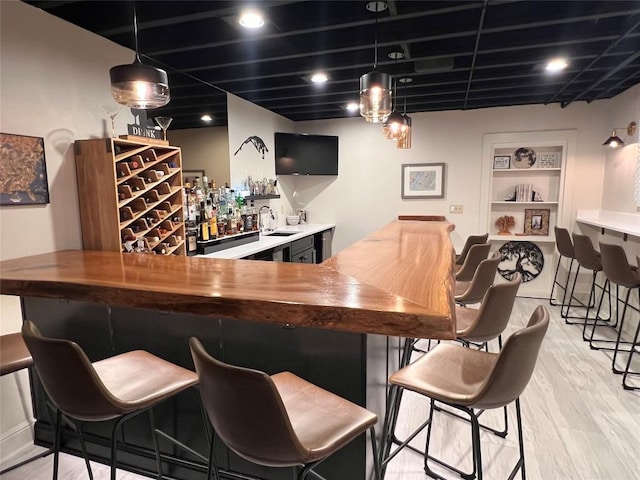 bar featuring pendant lighting, built in shelves, sink, and light hardwood / wood-style floors