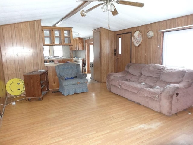 living room with vaulted ceiling with beams, wood walls, light wood-type flooring, and a healthy amount of sunlight