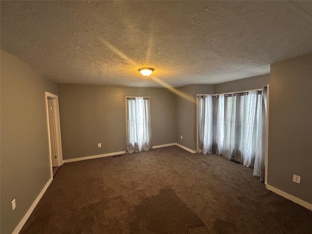 spare room featuring a textured ceiling and dark carpet