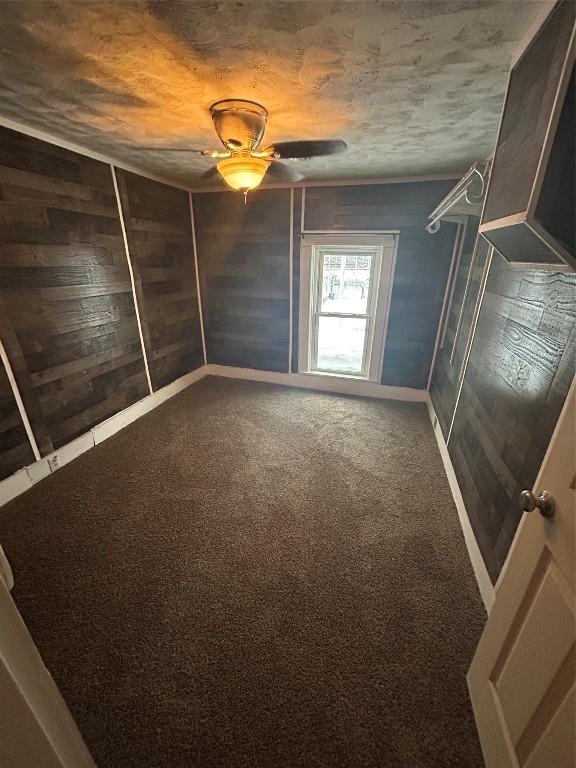 carpeted spare room with ceiling fan and wood walls