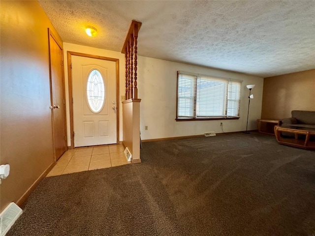 tiled foyer with carpet floors, visible vents, a textured ceiling, and baseboards