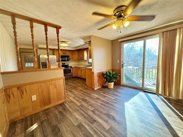 kitchen with a wainscoted wall, dark wood finished floors, light countertops, appliances with stainless steel finishes, and a peninsula