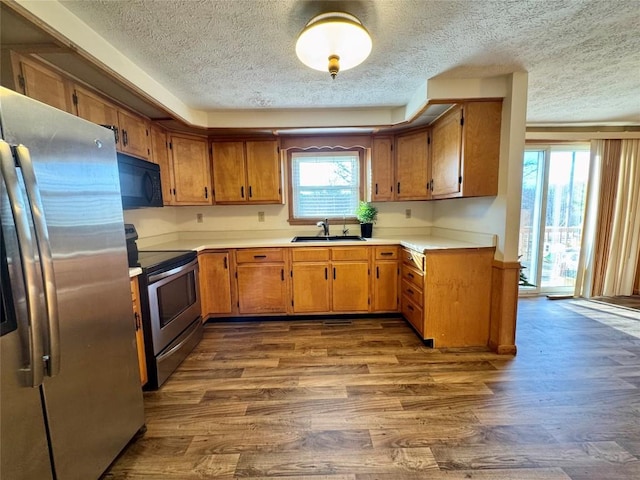 kitchen with dark wood finished floors, light countertops, appliances with stainless steel finishes, brown cabinetry, and a sink