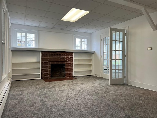 unfurnished living room featuring french doors, a brick fireplace, a drop ceiling, baseboard heating, and dark colored carpet