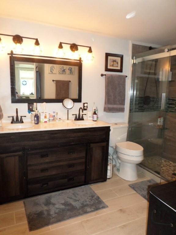 bathroom featuring a stall shower, toilet, and double vanity