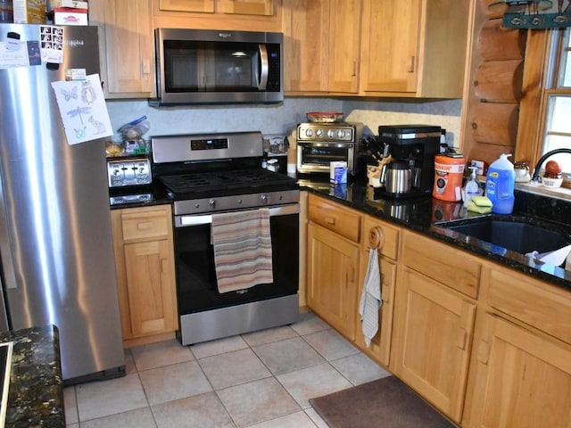 kitchen featuring appliances with stainless steel finishes, light tile patterned floors, dark stone countertops, and sink