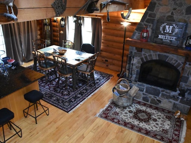 dining space featuring hardwood / wood-style floors, a stone fireplace, and log walls