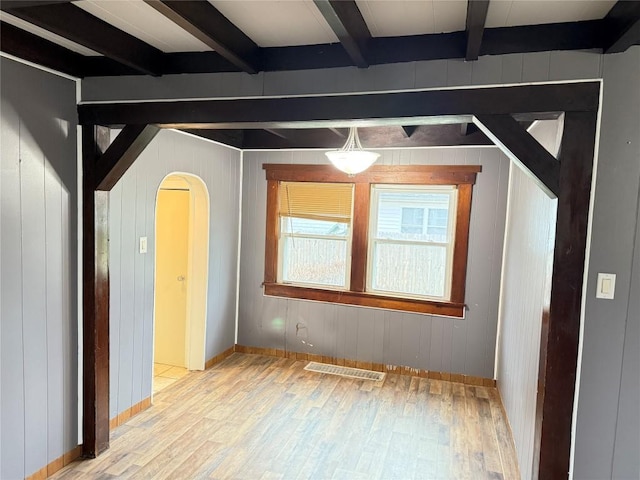 unfurnished room featuring wooden walls, beamed ceiling, and light hardwood / wood-style floors