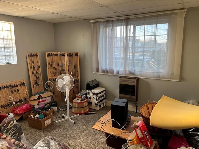 living area with heating unit, a paneled ceiling, carpet, and a healthy amount of sunlight