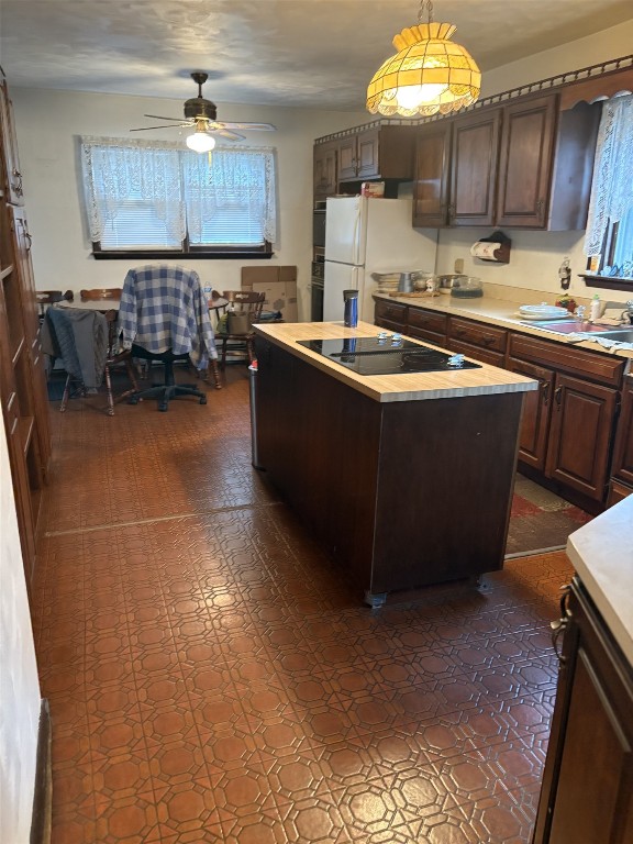 kitchen with black electric stovetop, freestanding refrigerator, light countertops, ceiling fan, and a center island