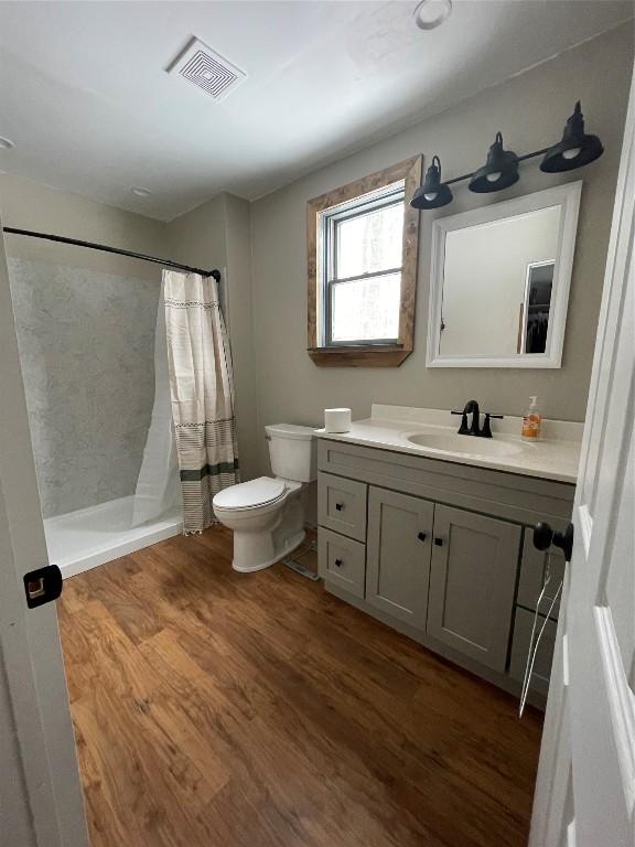 bathroom featuring curtained shower, visible vents, toilet, vanity, and wood finished floors