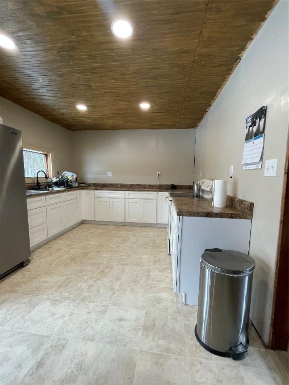 kitchen with dark countertops, wood ceiling, white cabinetry, and freestanding refrigerator