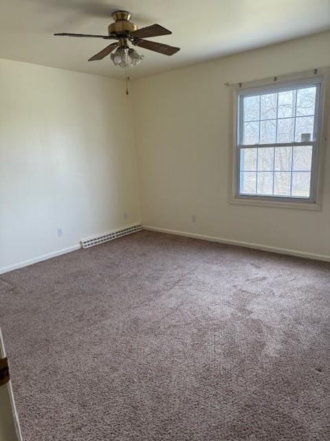 spare room featuring dark carpet, ceiling fan, baseboards, and a baseboard radiator