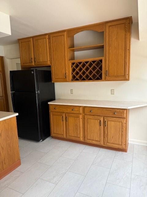 kitchen with open shelves, brown cabinets, light countertops, and freestanding refrigerator