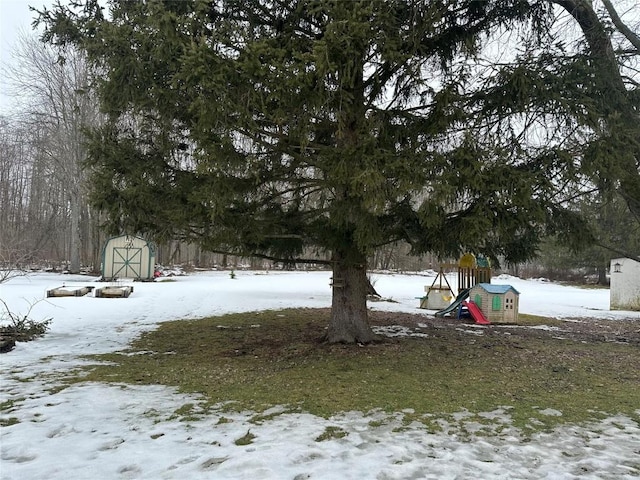 yard covered in snow featuring a storage unit, playground community, and an outbuilding