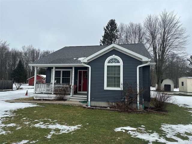 view of front facade featuring a yard, a porch, a shingled roof, and an outdoor structure