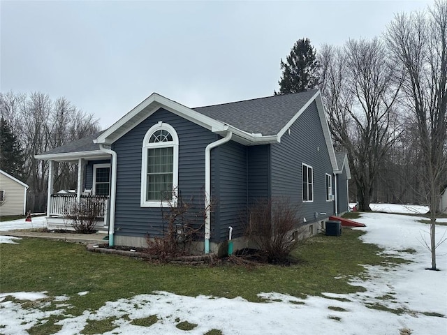 view of snow covered exterior with central air condition unit, a shingled roof, a porch, and a lawn