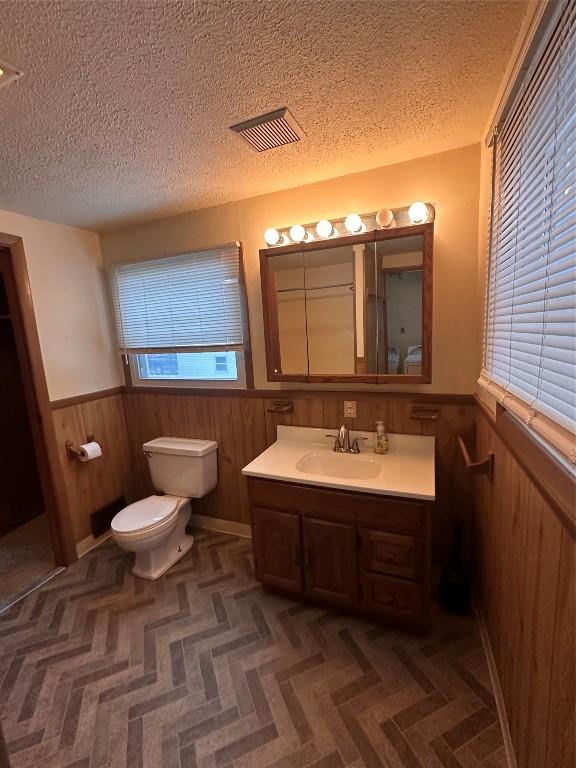 bathroom with vanity, wooden walls, toilet, and a textured ceiling