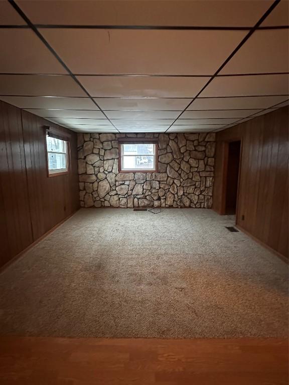 basement featuring a paneled ceiling, wooden walls, and carpet