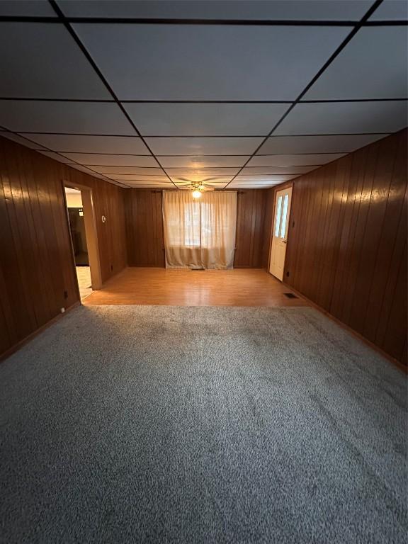 basement with a paneled ceiling, light carpet, and wood walls