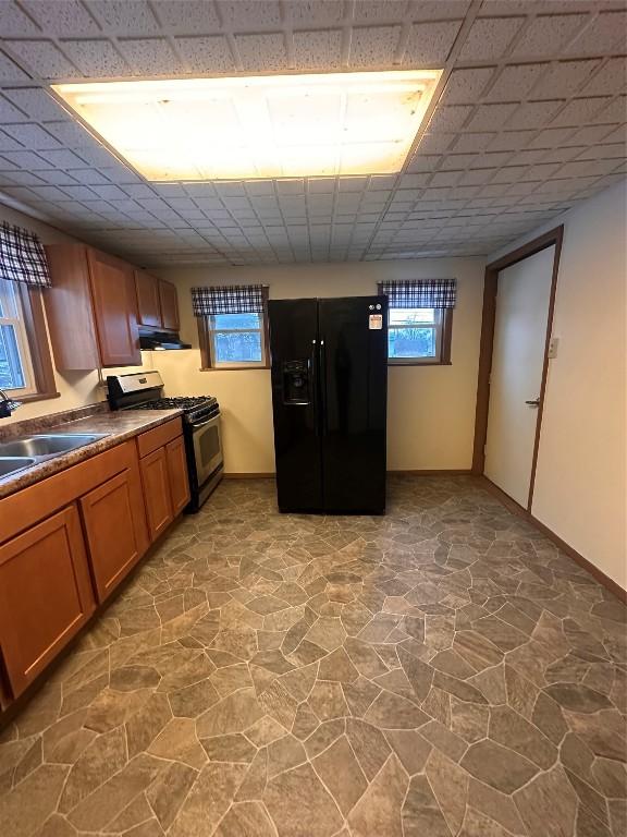 kitchen with a paneled ceiling, sink, stainless steel gas stove, and black refrigerator with ice dispenser