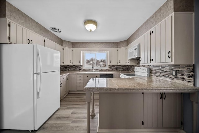 kitchen with tasteful backsplash, white appliances, sink, white cabinetry, and kitchen peninsula