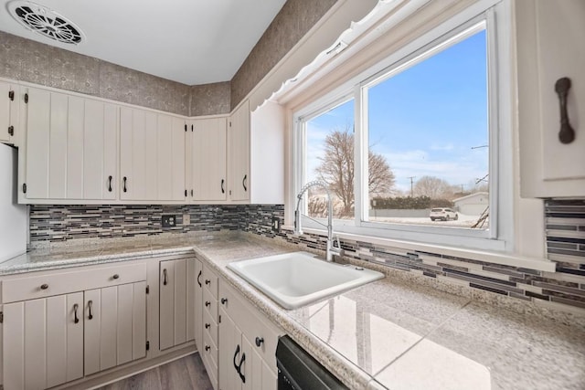 kitchen with hardwood / wood-style floors, sink, dishwasher, white cabinets, and decorative backsplash