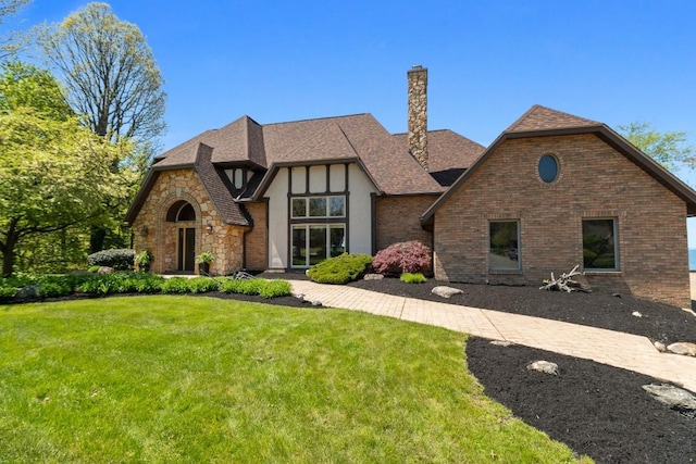 100 Fox Hollow Ln, Harborcreek, PA 16511 - tudor home featuring a front lawn, a chimney, stone siding, a shingled roof, and stucco siding