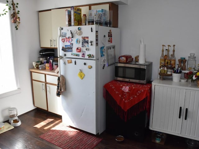 kitchen with stainless steel microwave, dark wood-type flooring, light countertops, and freestanding refrigerator